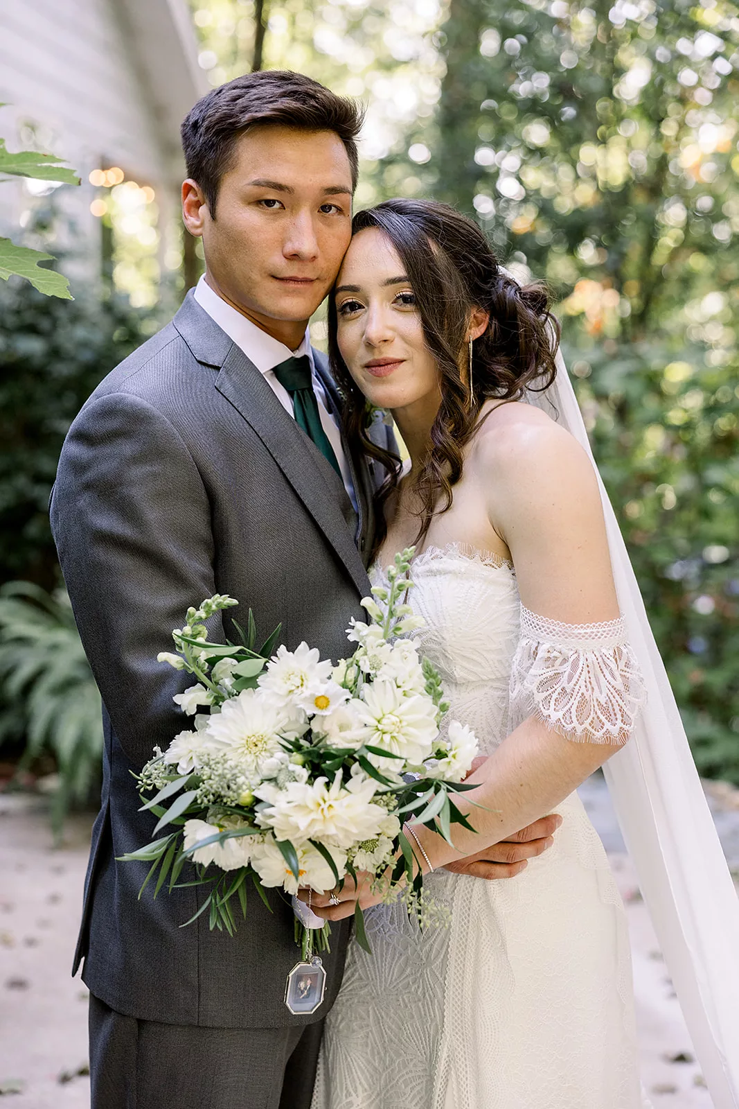 Newlyweds stand together holding a bouquet on the patio in the woods