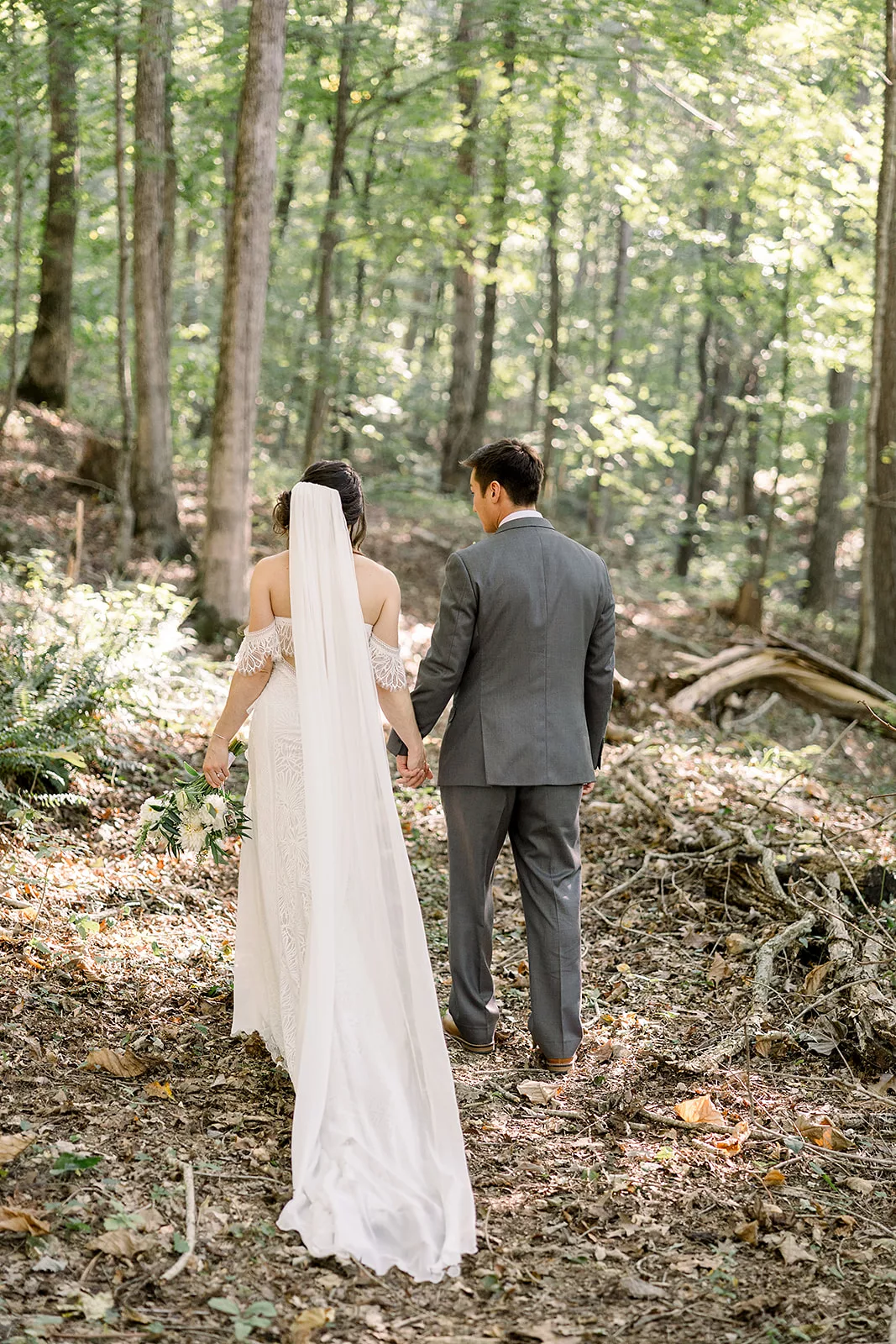 Newlyweds walk together holding hands up a forest trail