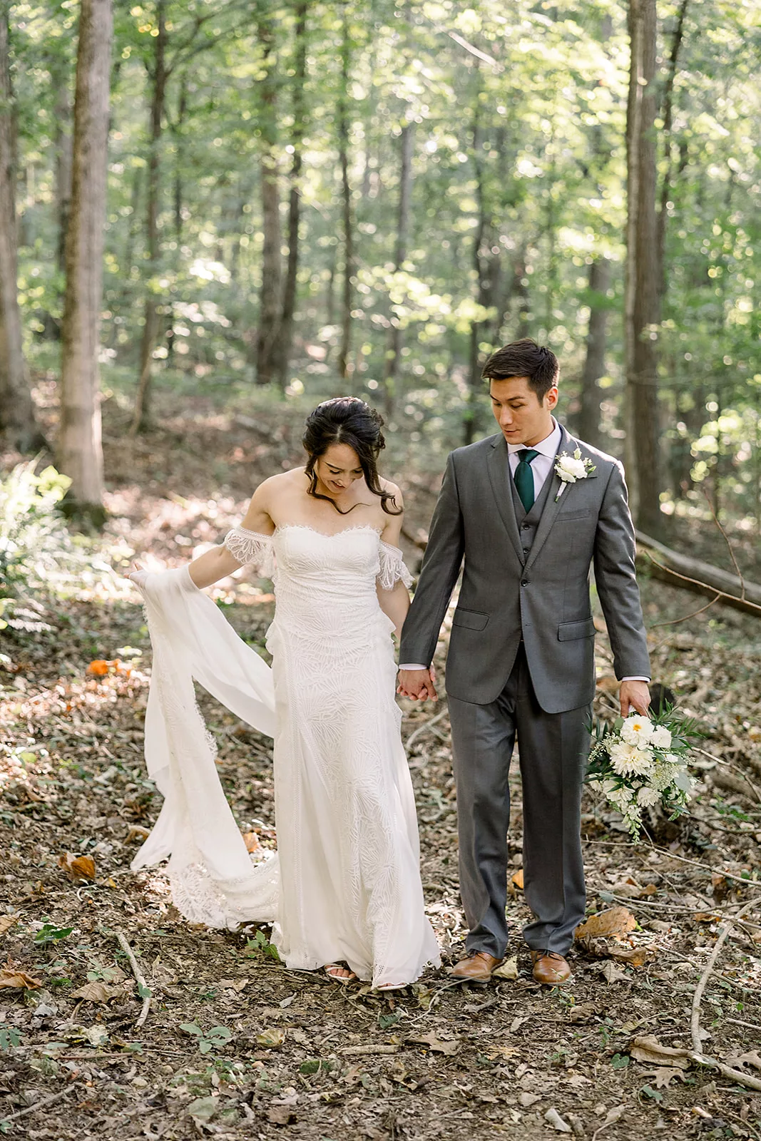 Newlyweds walk hand in hand through a forest trail at one of the best Sustainable Wedding Venue