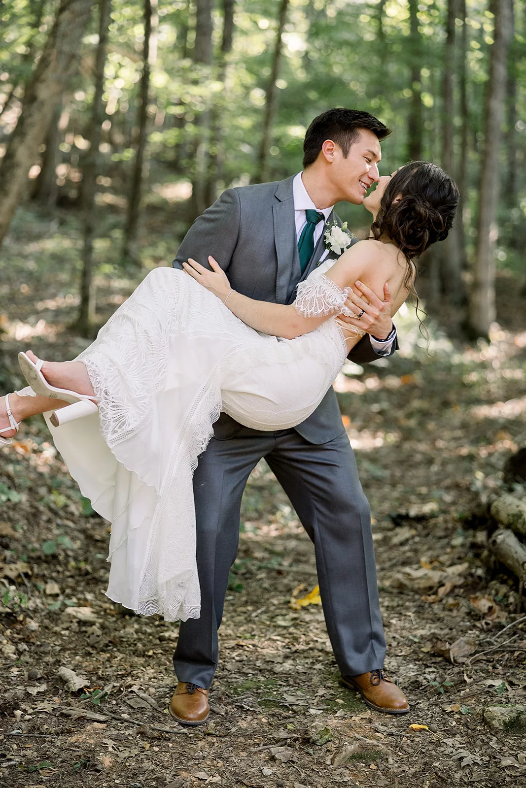 A groom lifts his bride and leans in for a kiss in the woods at a Sustainable Wedding Venue