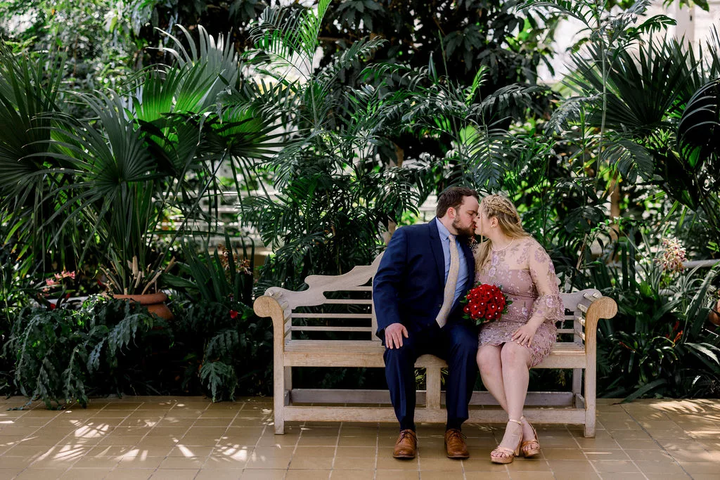Newlyweds kiss while sitting on a bench in a uga botanical gardens wedding