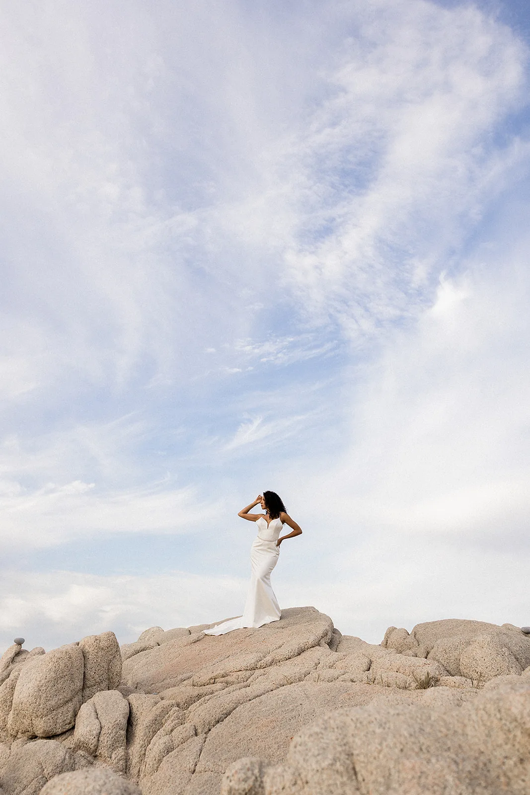 A bride stands on a rock formation on the beach at her Grand Velas Los Cabos Wedding