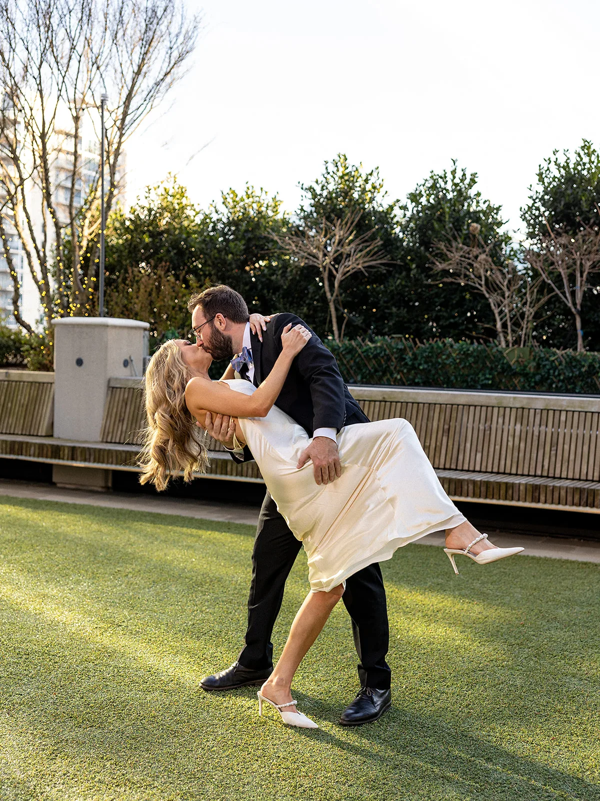 A groom dips and kisses his bride on a rooftop terrace at sunset