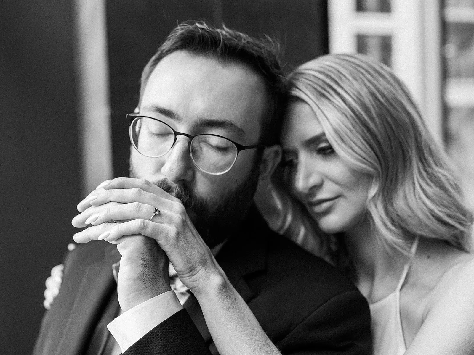 A groom kisses the hand of his bride as they snuggle in black and white