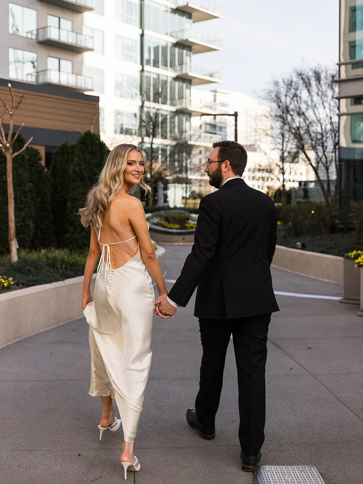 A bride smiles over her shoulder while walking through a garden holding hands with her groom