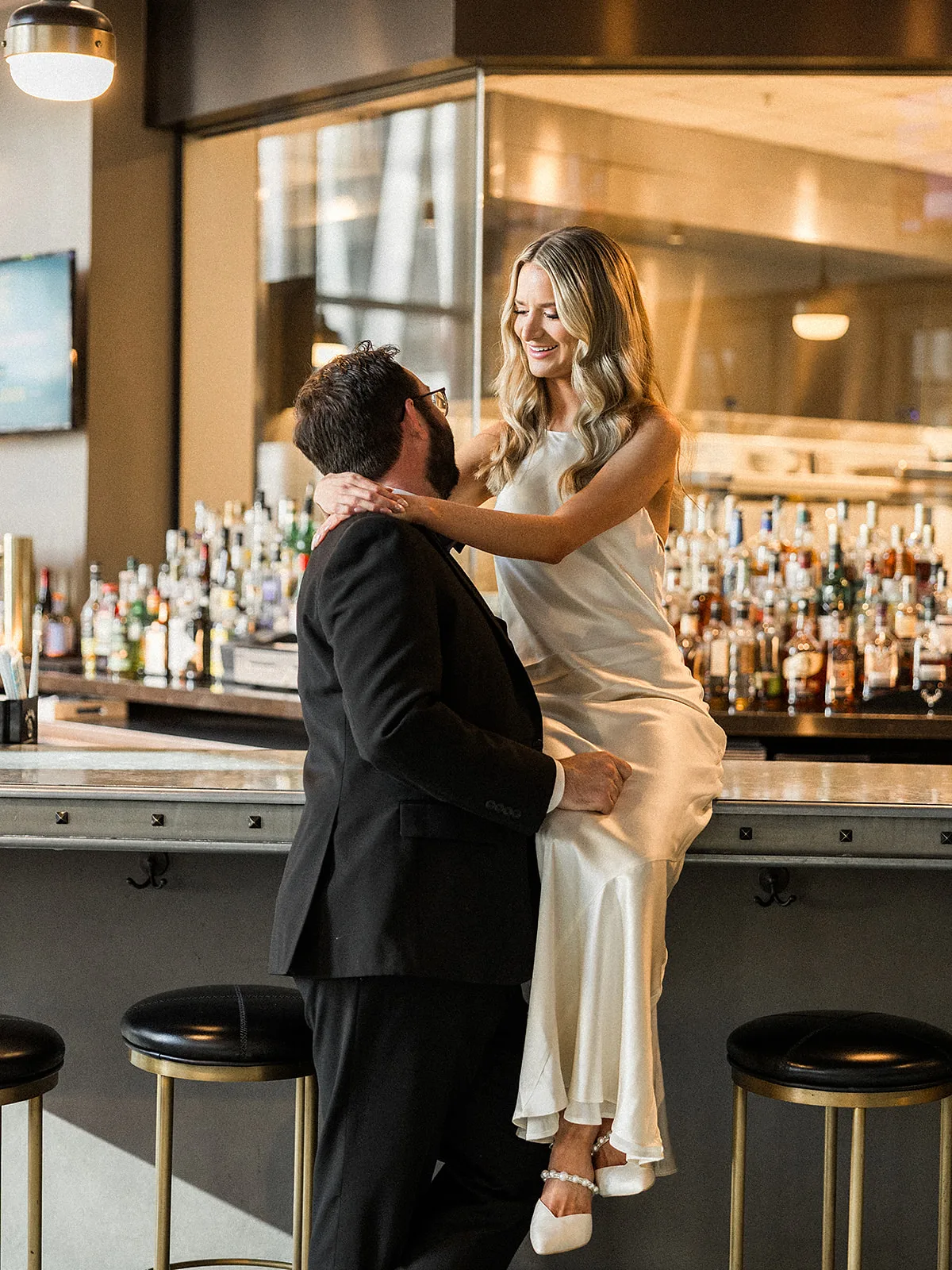 A bride sits on an Epicurian Atlanta bar hugging onto her groom