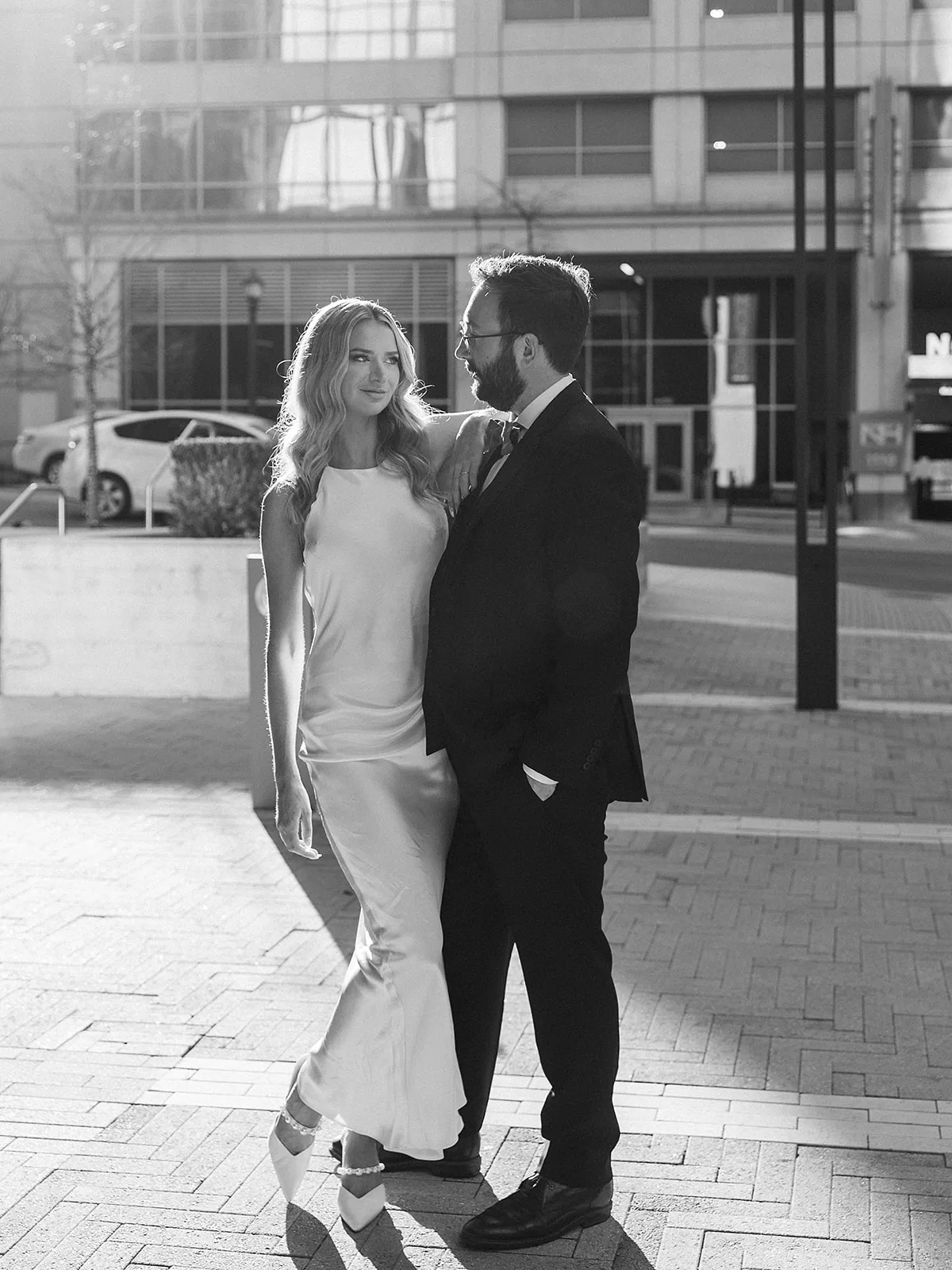 A bride leans on her groom as they stand on a metro street