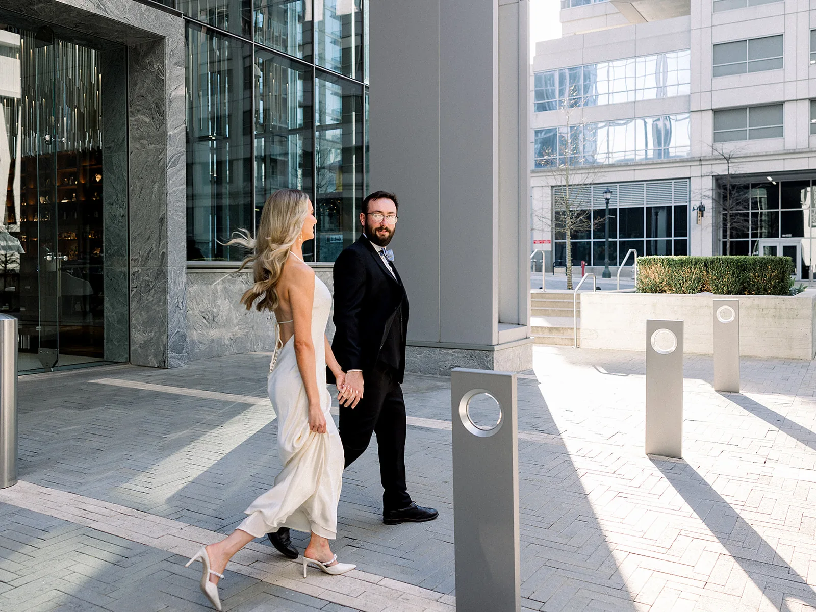 A groom walks with his bride holding hands outside the front entrance of the Epicurian Atlanta at sunset